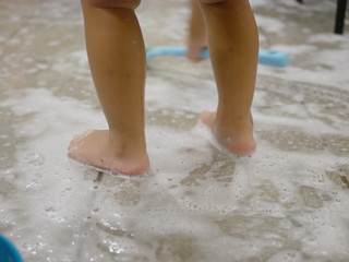 White foam and air bubbles at baby's feet on the bathroom floor, as she is haveing fun learning to clean a restroom - children development through allowing them to do housework