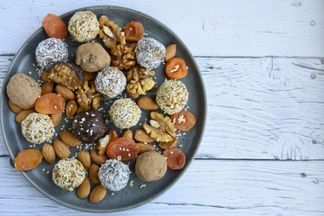 energy balls, almonds, walnuts, dried apricots on a gray plate and wooden white background