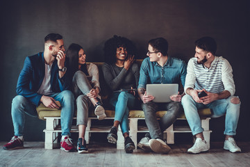 Happy diverse friends group sharing social media app news sitting holding phones, smiling multiracial young people students showing funny videos on laptop