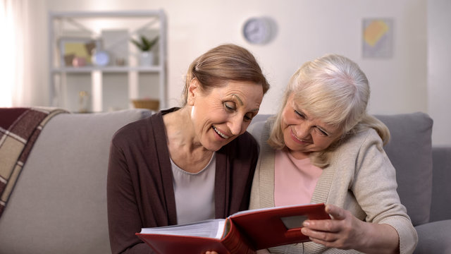 Happy female pensioners admiring old photos in album, retirement leisure, fun