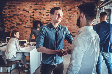 Two happy young men shaking hands while standing in the office