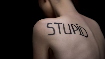 Naked woman turned from camera, word stupid on shoulder, bullying problem