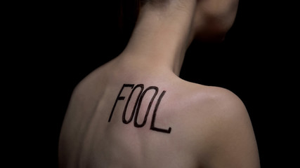 Naked woman turned from camera, word fool on shoulder, public opinion, bullying