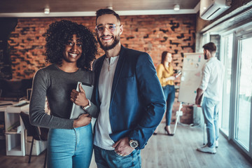 Obraz premium Portrait of young man and woman standing in office with colleagues meeting in background.