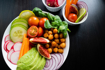 Buddha bowl with avocado, chickpeas, red onion, cucumber, tomatoes, radish and natural rice on a dark wooden table. Top view.