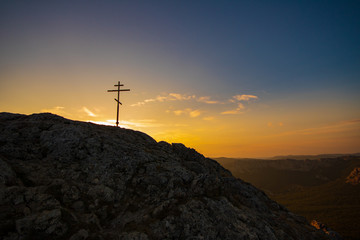 Religious cross on the mountain. View on sunset sky and mountains.