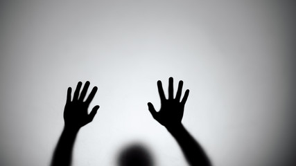 Silhouette of hands sliding down glass wall, person dying, crime scene, horror