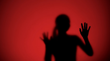 Female silhouette behind glass escaping from danger, red lights on background