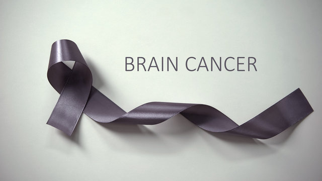 Brain cancer inscription, gray ribbon lying on table, awareness campaign, ad
