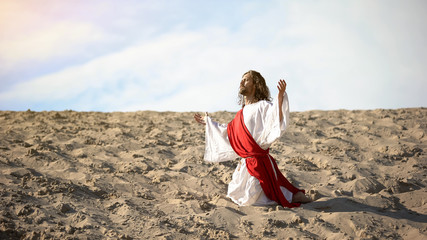 Righteous man kneeling in desert, praying to god with raised hands, confession