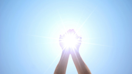 Hands holding sacred light against blue sky, religious miracle, ray of hope