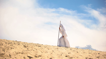 Tired Bedouin with staff walking in hot desert, climate change, global warming