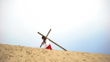 Jesus falling under heavy wooden cross, suffering pain and exhaustion, sacrifice