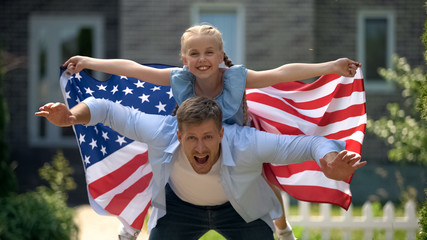 Excited dad and girl patriots having fun, holding USA flag, family immigration