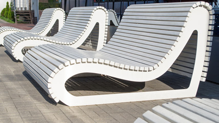 A row of white wooden unusual benches of modern design, streamlined rounded shape, reminiscent of a...