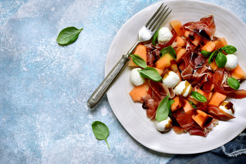 Delicious salad with melon, prosciutto or jamon and mozzarella cheese. Top view with copy space.