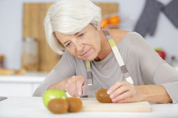 Obraz na płótnie Canvas senior woman cutting vegetables in kitchen