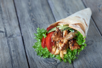 Shawarma rolled in lavash, moist grilled meat with onion, herbs and vegetables on wooden background.