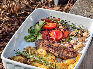 Barbecued vegetables and steaks in white ceramic bowl.