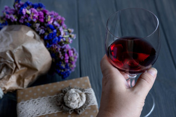 A glass of red wine close-up along with a bouquet of wildflowers and gift boxes on a dark wooden background. Birthday greeting card banner design.