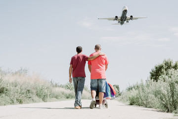 couple of gay men walk together with a child's car, in the sky there is a plane.LGTB,LGBT