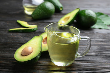 Jug of natural oil and avocados on dark wooden background