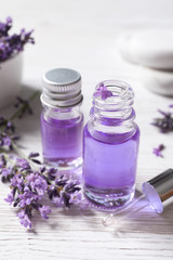 Glass bottles of natural cosmetic oil and lavender flowers on white wooden table