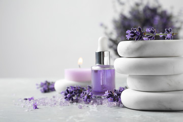 Spa stones, natural cosmetic oil and lavender flowers on grey table, space for text