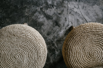 Fototapeta na wymiar Natural straw round pouf cushion chair with wooden legs, grey concrete floor. Close up details. Minimalist loft coffee shop, restaurant, home interior design