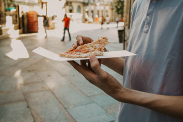 hands with slice of pizza on urban street outdoors