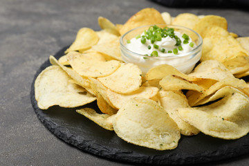 Sour cream in dipping saucer and chips on grey stone background