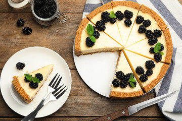 Sliced delicious cheesecake with blackberries on wooden background, flat lay
