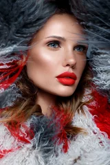 Schöne Frau mit klassischem Urlaubs-Make-up, roten Lippen, Locken in einem mehrfarbigen Lama-Mantel. Schönes Gesicht. © Kobrinphoto
