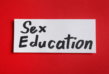 Piece of paper with phrase "SEX EDUCATION" on red background, top view