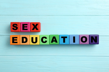 Colorful wooden blocks with phrase "SEX EDUCATION" on light blue background, flat lay