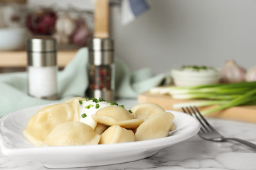 Delicious cooked dumplings with sour cream on white marble table, closeup