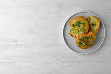 Slices of toasted bread with garlic and herbs on white wooden table, top view. Space for text