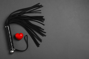 Black whip and red heart on dark background, flat lay with space for text. Sexual role play...