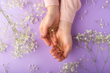 Flat lay. Tender female hands with white delicate flowers. On a purple background. Art photo, top view, horizontal photo.