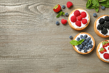Different berry tarts on wooden table, flat lay with space for text. Delicious pastries