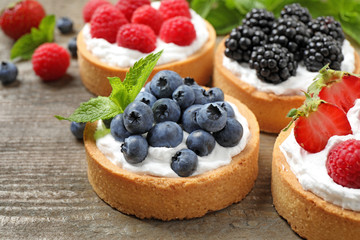 Different berry tarts on wooden table, closeup. Delicious pastries