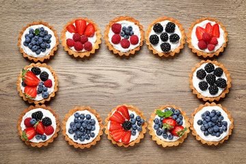 Frame made with different berry tarts on wooden table, space for text. Delicious pastries
