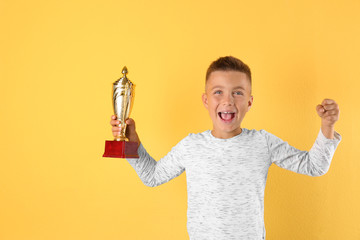 Happy boy with golden winning cup on yellow background