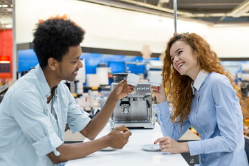 Obraz premium African curly-haired man with a red-haired girl drinking freshly brewed coffee testing coffee machines in the store