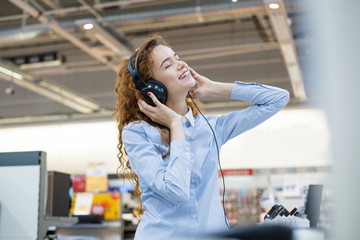 Redhead girl tests new full-size headphones while standing in store
