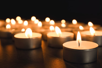 Fototapeta na wymiar Burning candles on table in darkness, closeup. Funeral symbol
