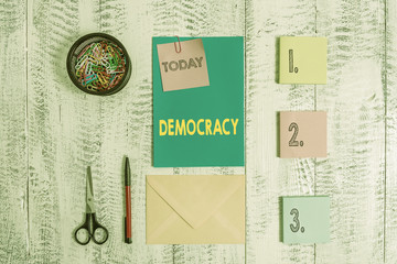 Word writing text Democracy. Business photo showcasing freedom of the showing to express their feelings and beliefs Envelope letter sticky note ballpoint clips can scissors wooden background