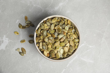 Bowl of raw pumpkin seeds on light grey marble table, top view