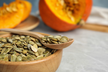 Bowl and spoon of raw pumpkin seeds on light grey table, closeup. Space for text