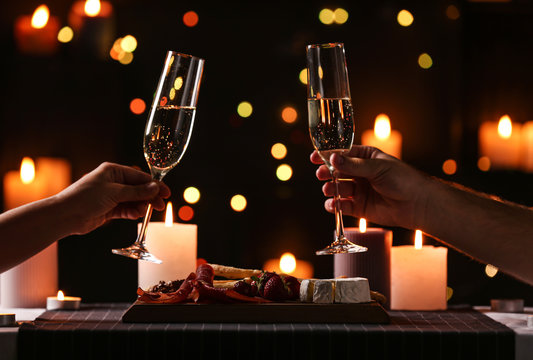 Young couple with glasses of champagne having romantic candlelight dinner at table, closeup